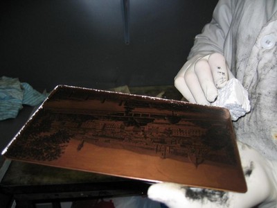 The artist uses the edge of the plate to scrape a powdery deposit from a block of magnesium carbonate